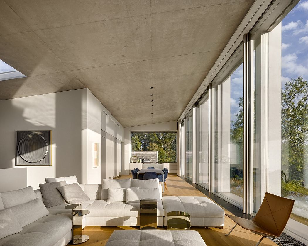 Spacious modern interior with large windows, minimalist furniture, and concrete ceiling.