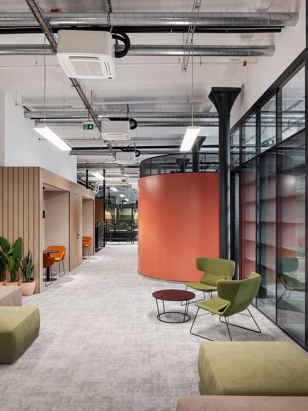 A modern, spacious office interior featuring colorful furniture, a curved orange wall, and an exposed industrial ceiling.
