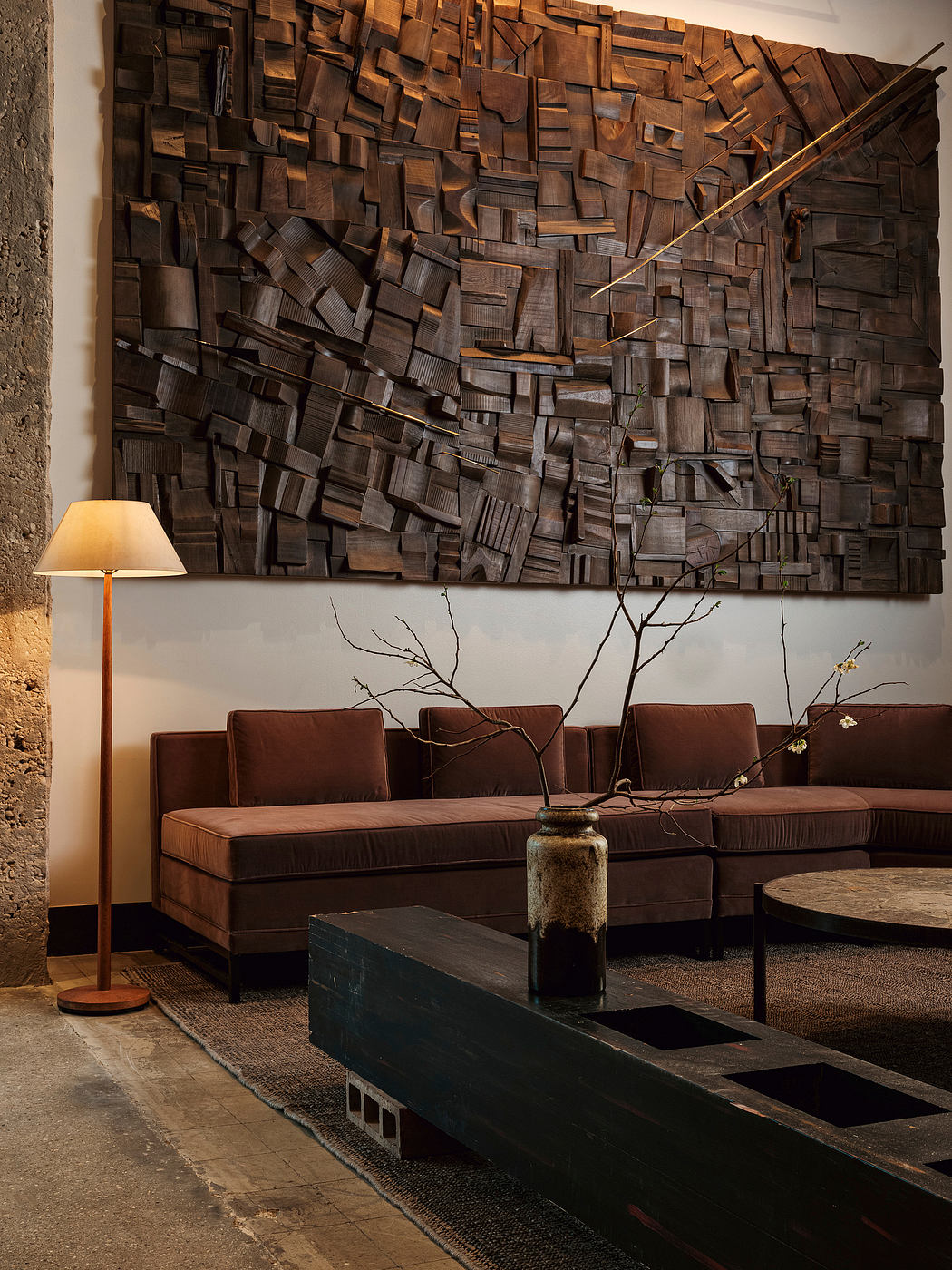 A rustic wood wall sculpture, leather sofa, and modern coffee table create a cozy, industrial-chic space.