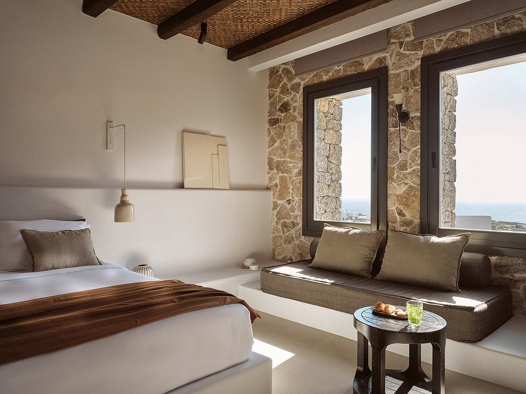 Rustic bedroom with stone walls, wood beams, and a cozy seating area overlooking the view.