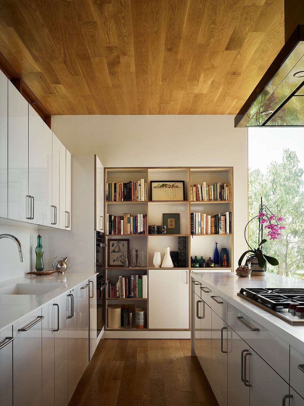 Sleek, modern kitchen with built-in shelving, wood-beamed ceiling, and large window.