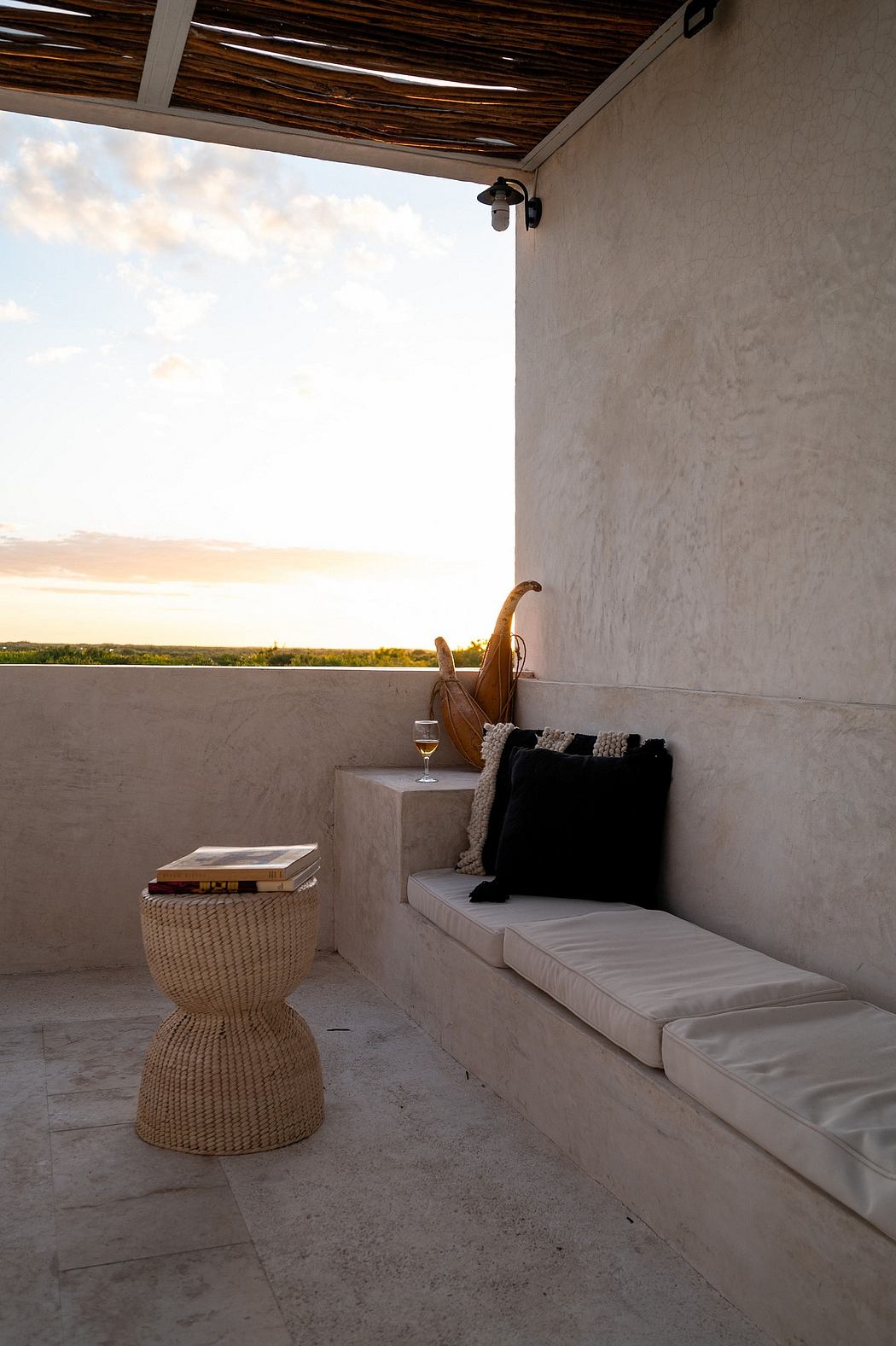 Cozy outdoor seating area with wooden ceiling, gray wall, cushioned bench, and woven side table.