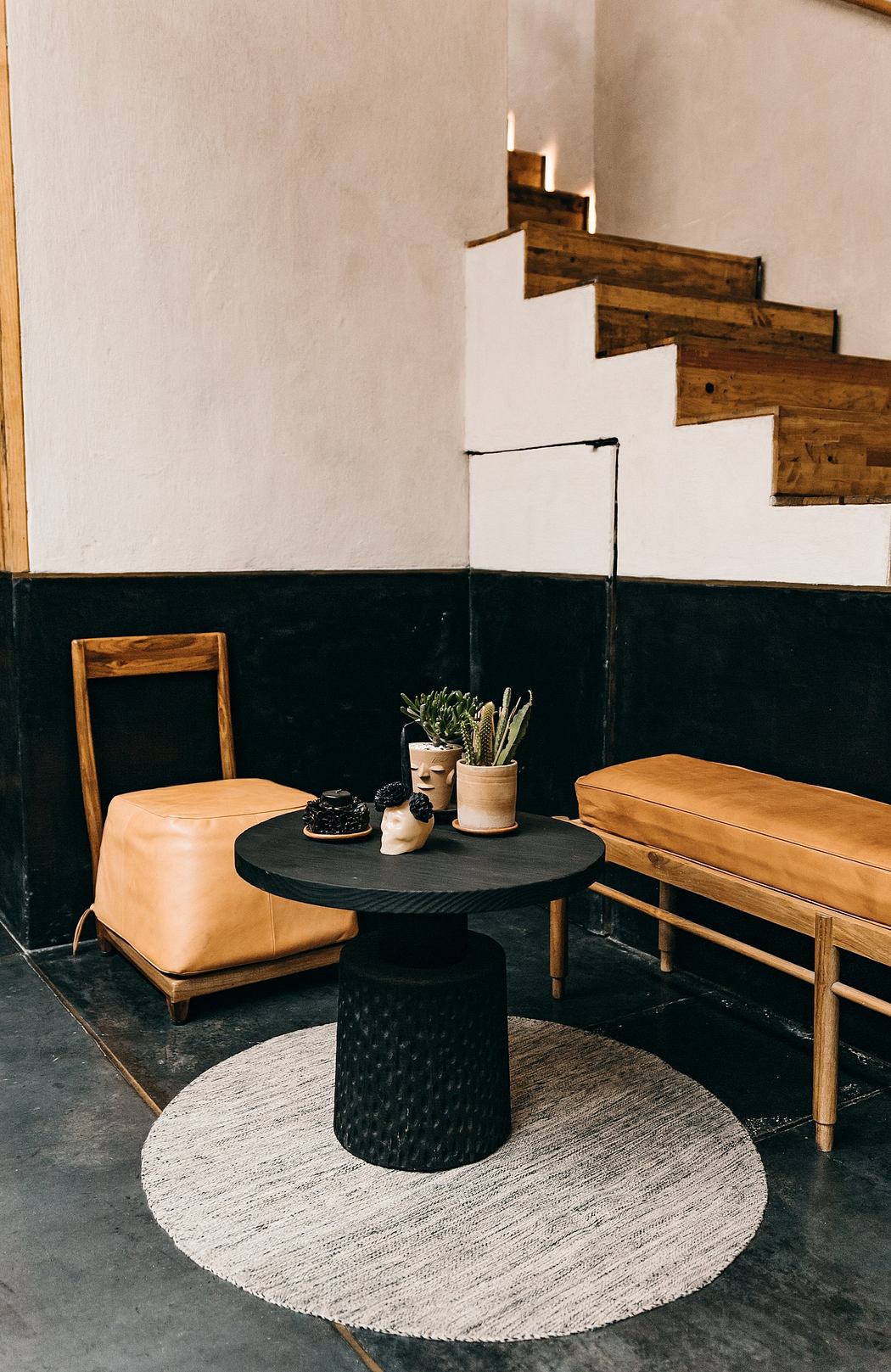 The image showcases a modern, minimalist interior design with a wooden staircase, leather seating, and a round coffee table on a circular rug.