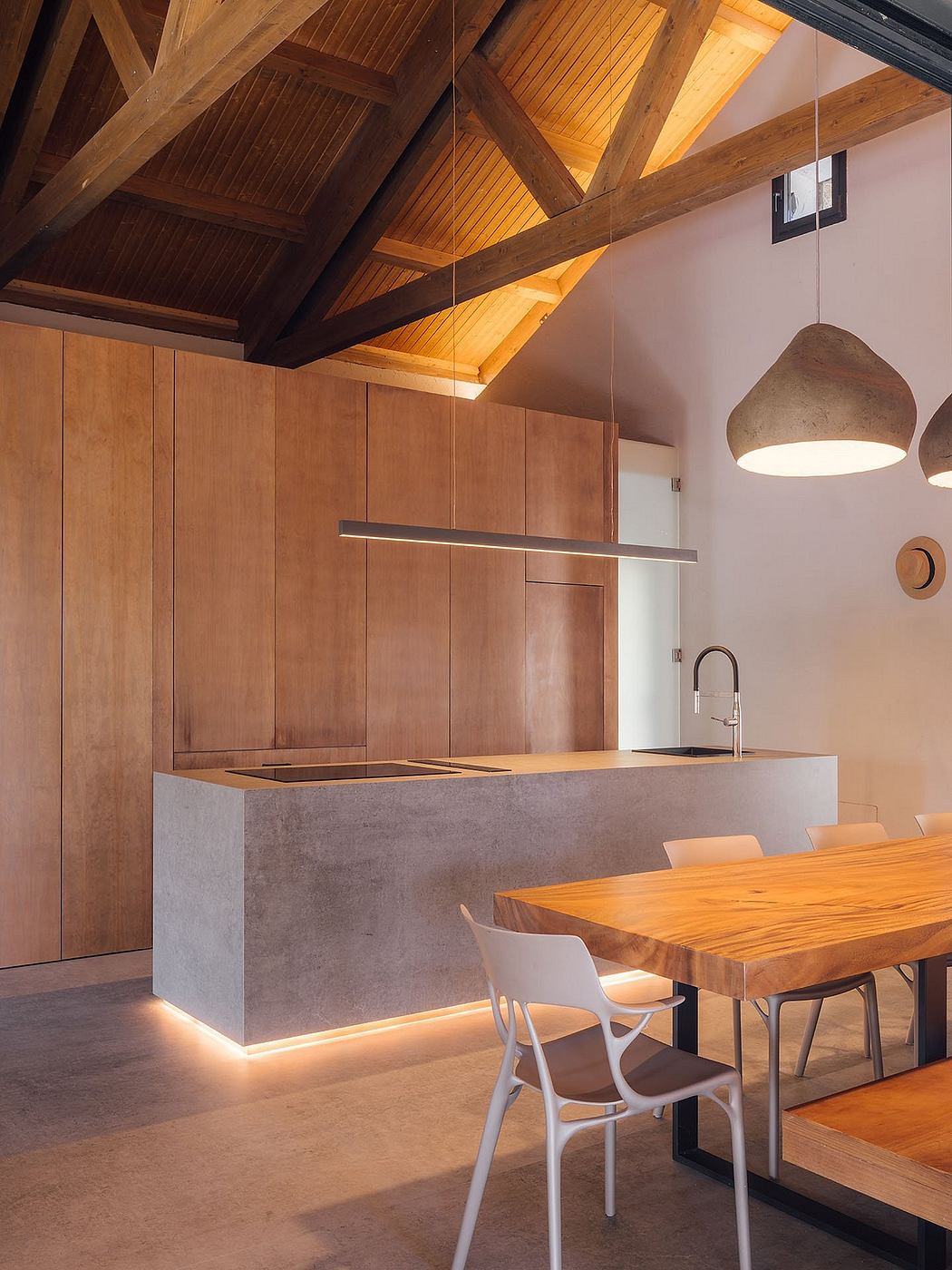 Warm wooden beams, concrete counters, and a rustic dining table in a modern kitchen.