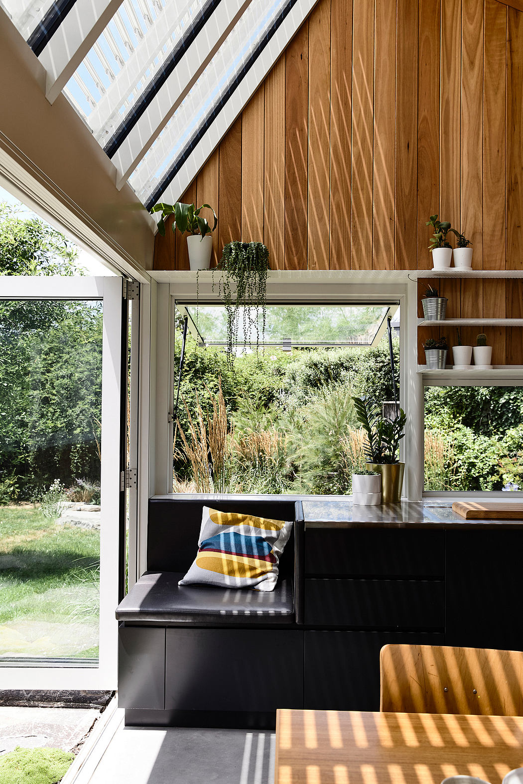 A cozy indoor-outdoor living space with wood paneling, shelves, and a comfortable seating area overlooking lush greenery.