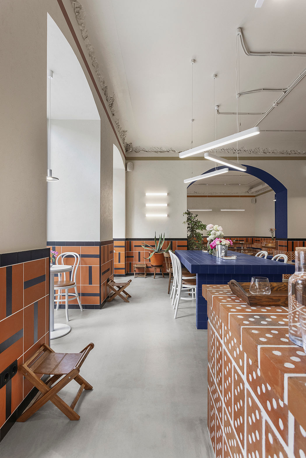 A modern, vibrant interior with geometric tile patterns, pendant lights, and a central dining table.