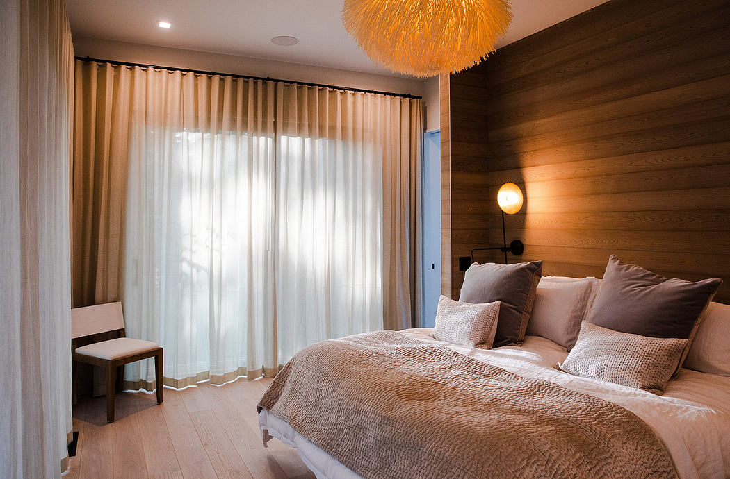 Warm, inviting bedroom with wood-paneled walls, sheer curtains, and an eye-catching orange light fixture.