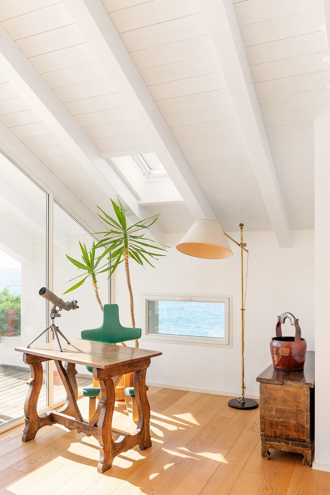 Airy modern room with high vaulted ceiling, rustic wooden table, and views of the water.