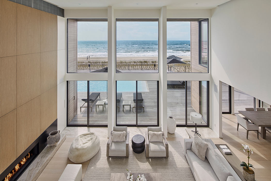 Expansive beachfront living room with floor-to-ceiling windows, minimalist furnishings, and deck.