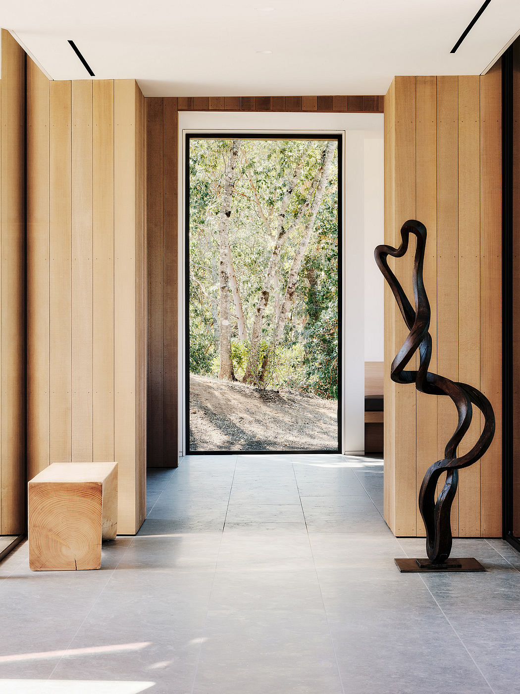 A modern interior design with wooden paneling, marble floors, and a large window framing a lush forest view.
