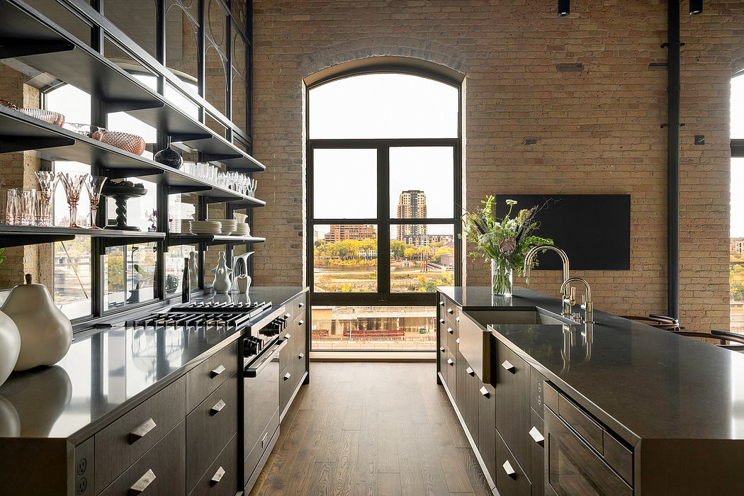 Modern industrial-style kitchen with exposed brick walls, floor-to-ceiling windows, and sleek stainless steel cabinetry.
