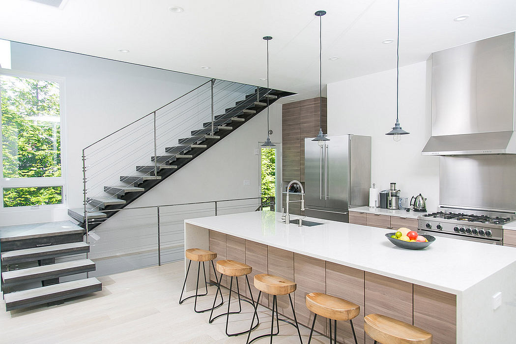 This sleek, modern kitchen features a minimalist staircase, stainless steel appliances, and an expansive island countertop.