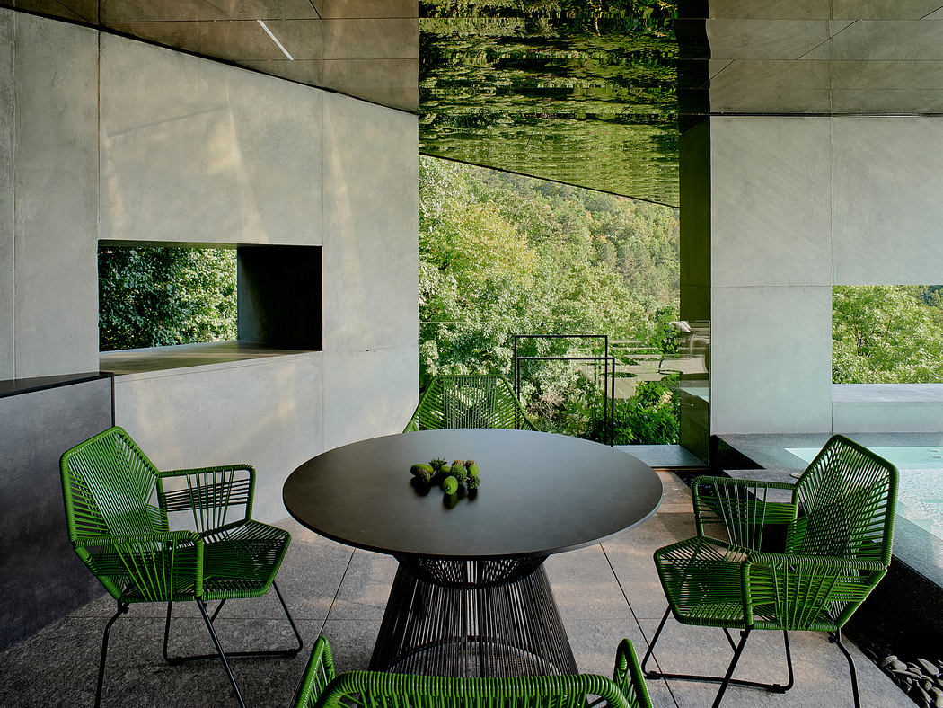 A modern outdoor seating area with a black circular table and vibrant green chairs overlooking a lush forest.