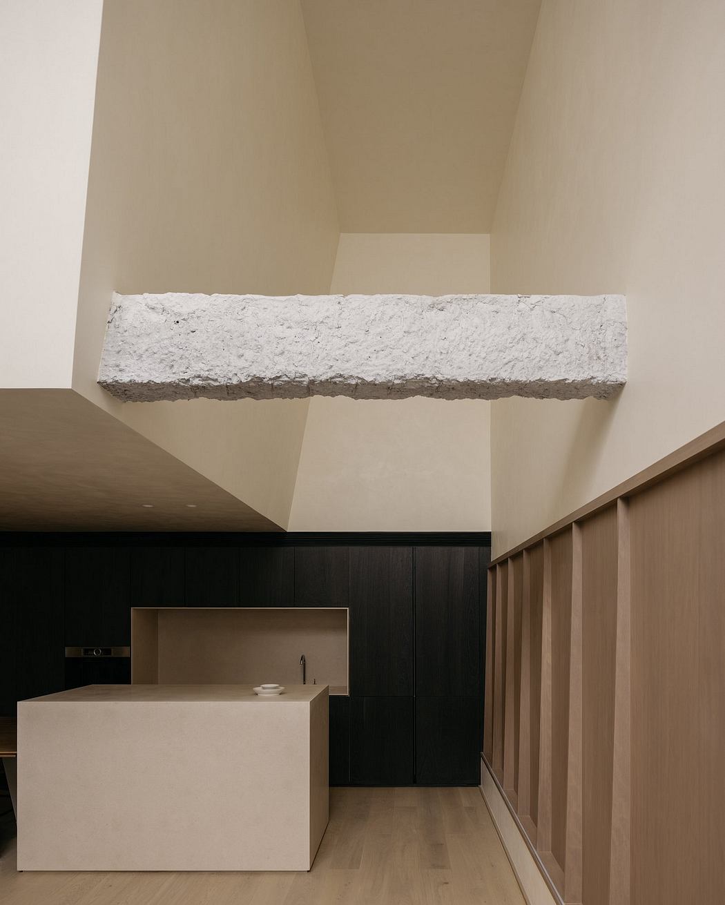 Minimalist kitchen design with sleek black cabinetry, white marble countertop, and exposed concrete beam.
