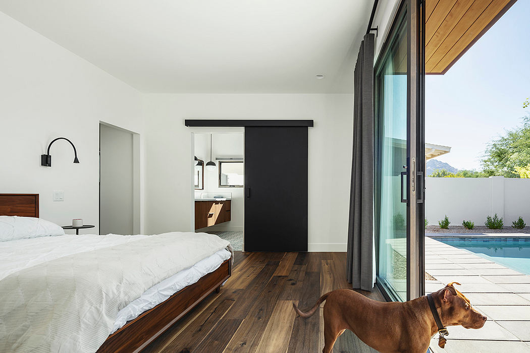 Sleek, minimalist bedroom with sliding black door, wooden floors, and outdoor pool view.