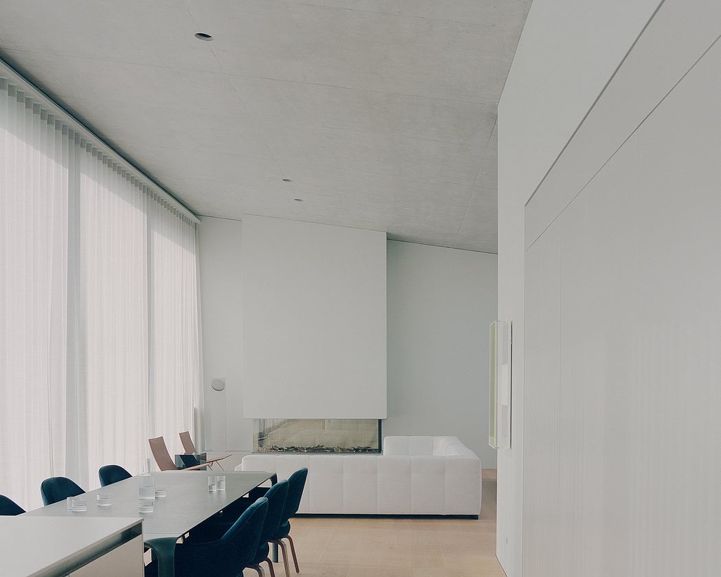 Minimalist room with white walls, concrete ceiling, and large window overlooking a seating area.
