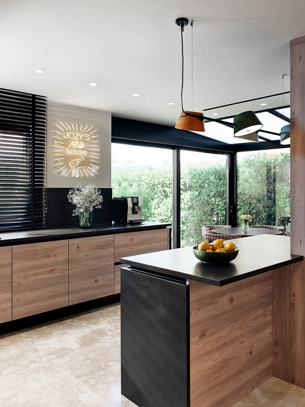 Modern kitchen with sleek black and wood cabinetry, pendant lights, and lush greenery outside.