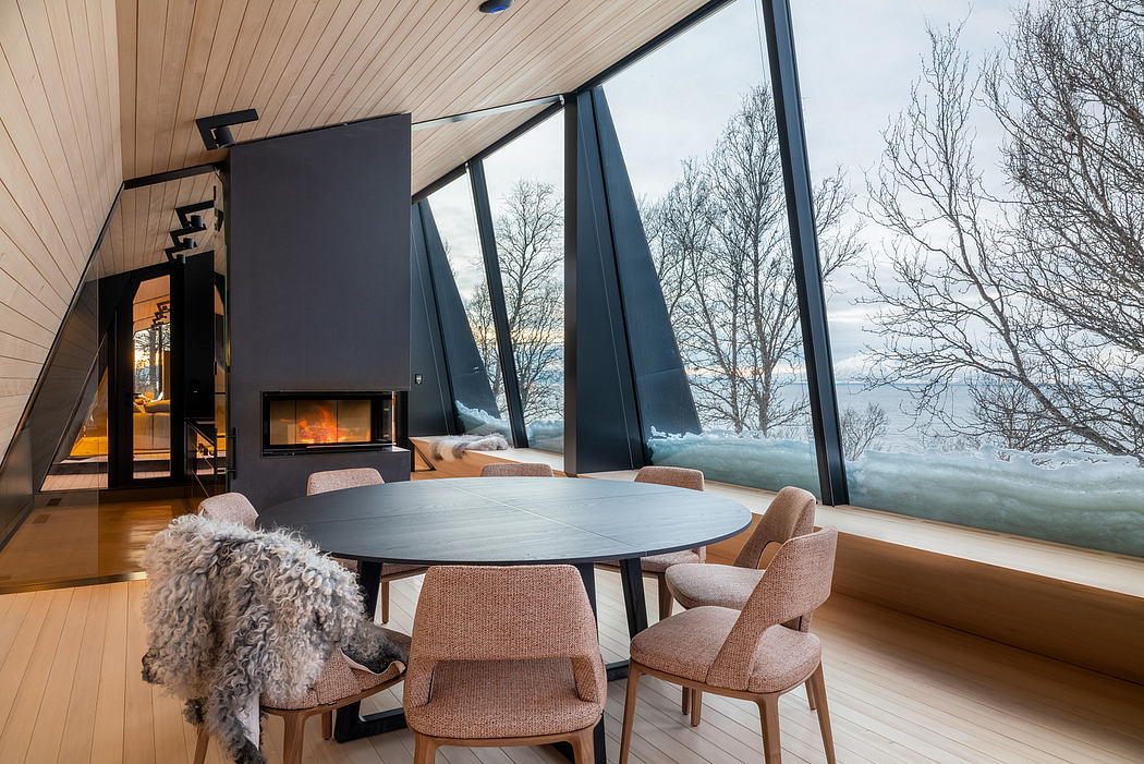 A modern cabin interior with a fireplace, large windows, and a round dining table surrounded by chairs.