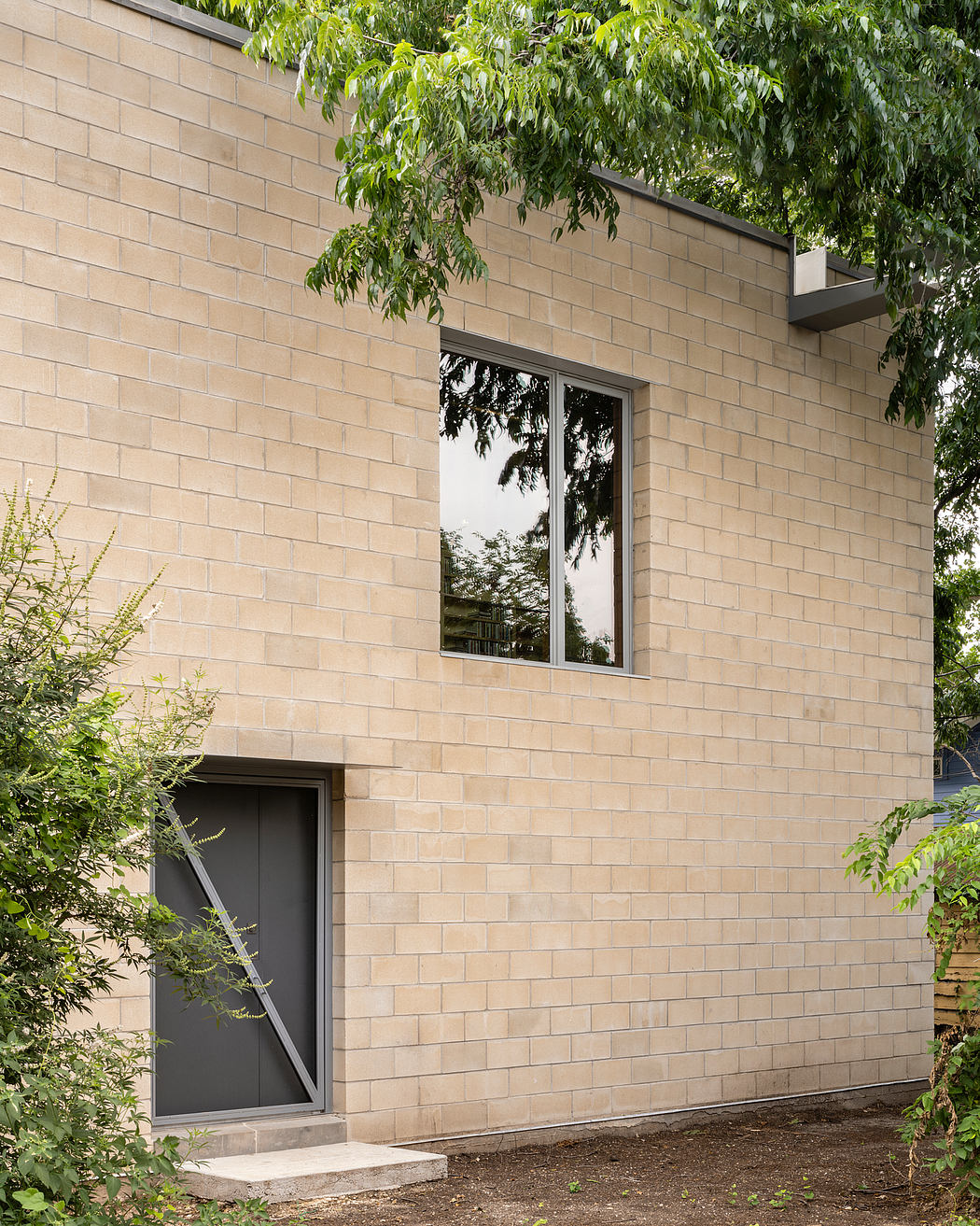 A modern brick building with a large window reflecting the surrounding foliage.