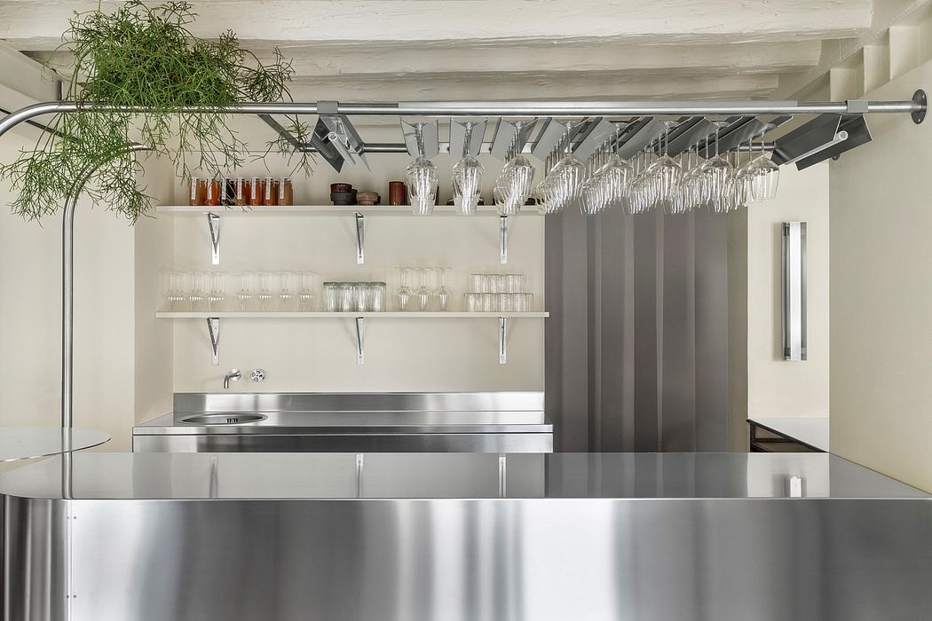 Modern, minimalist kitchen with stainless steel countertops, shelving, and hanging stemware.