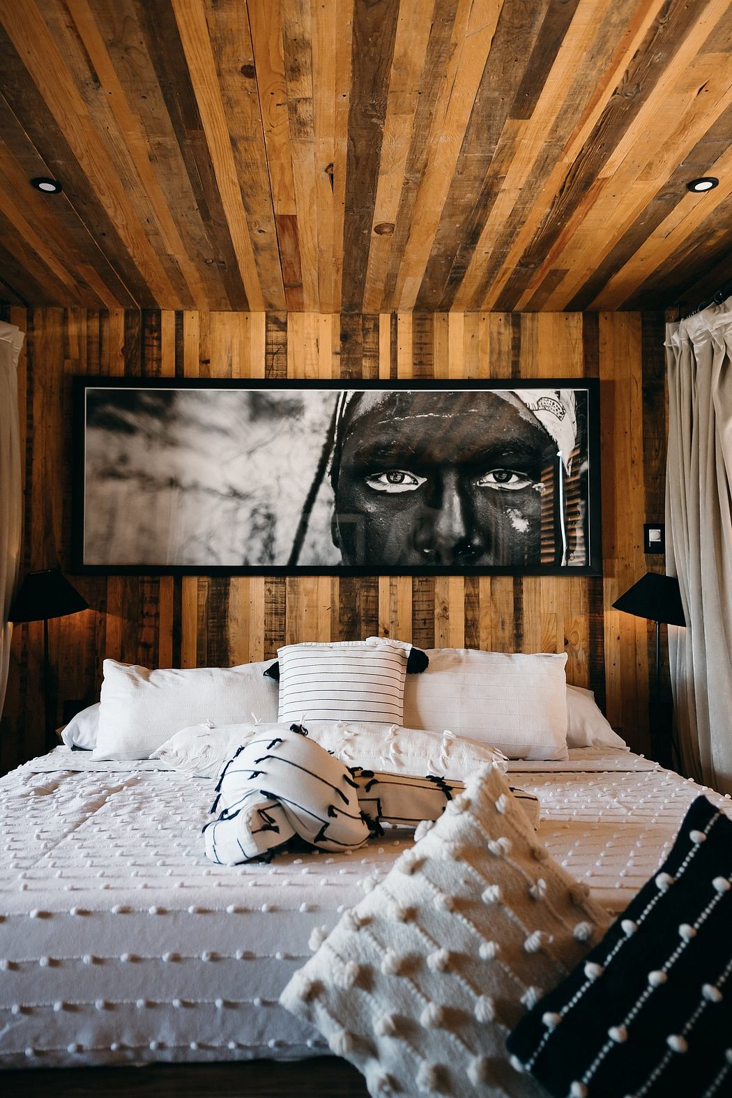 Rustic wooden walls and ceiling frame a large black-and-white portrait above the bed.