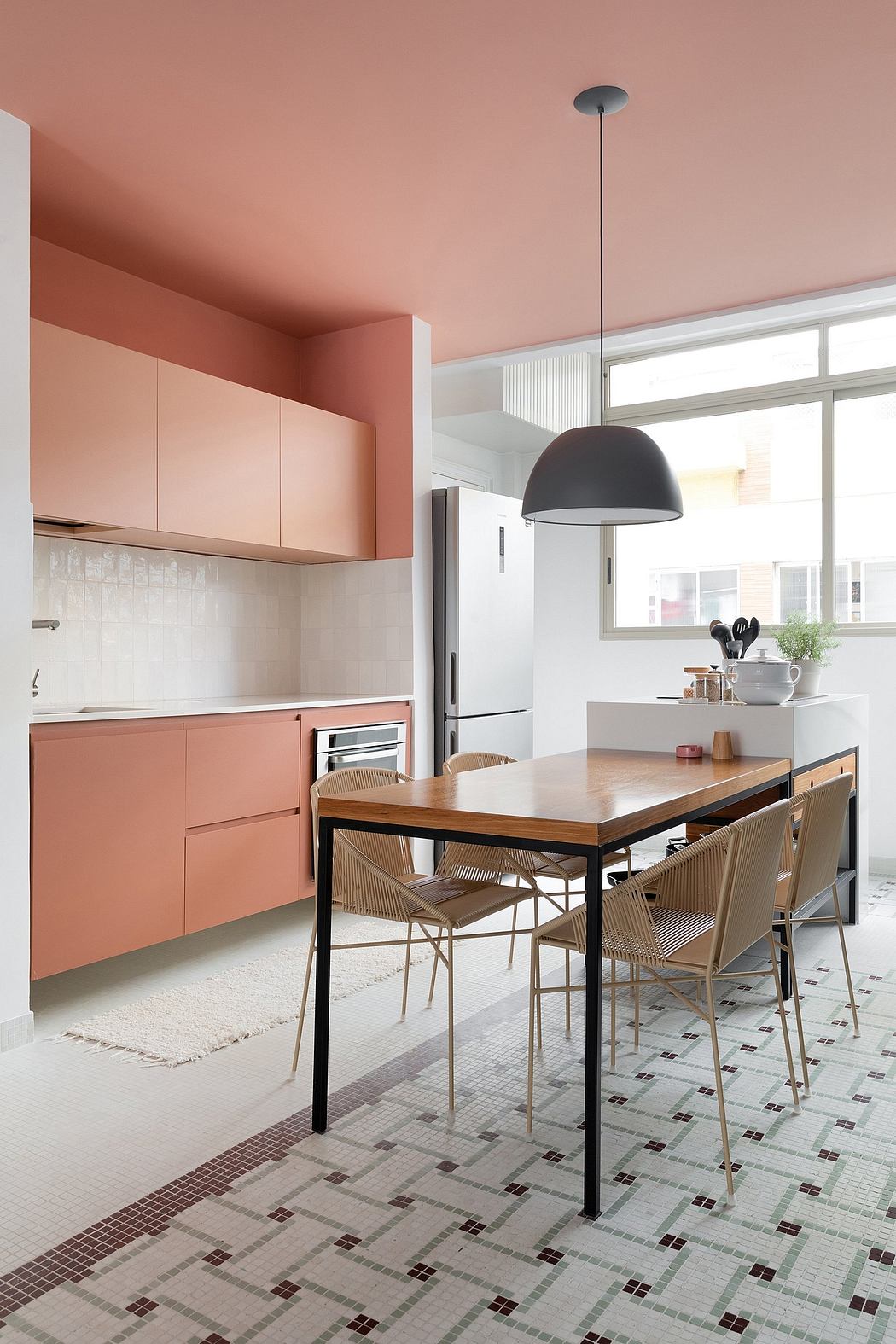 Modern kitchen with coral-colored cabinets, wooden table, and geometric tile floor.