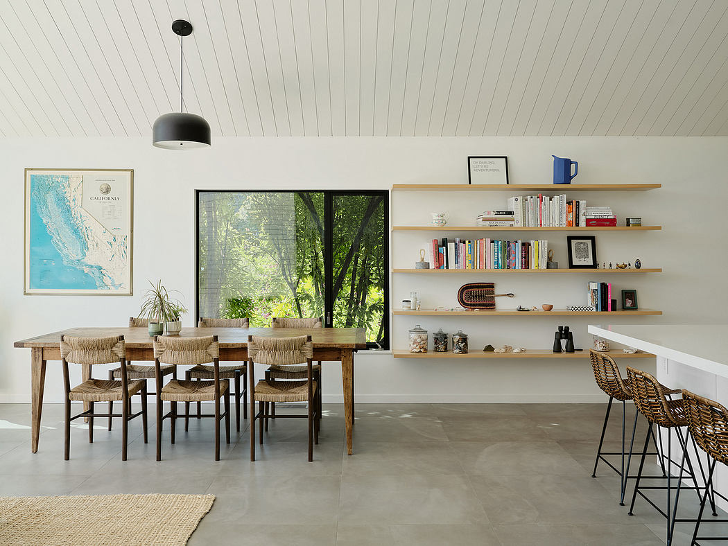 A modern, open-concept dining area with natural wood furniture, shelving, and large windows overlooking a lush, forested scene.