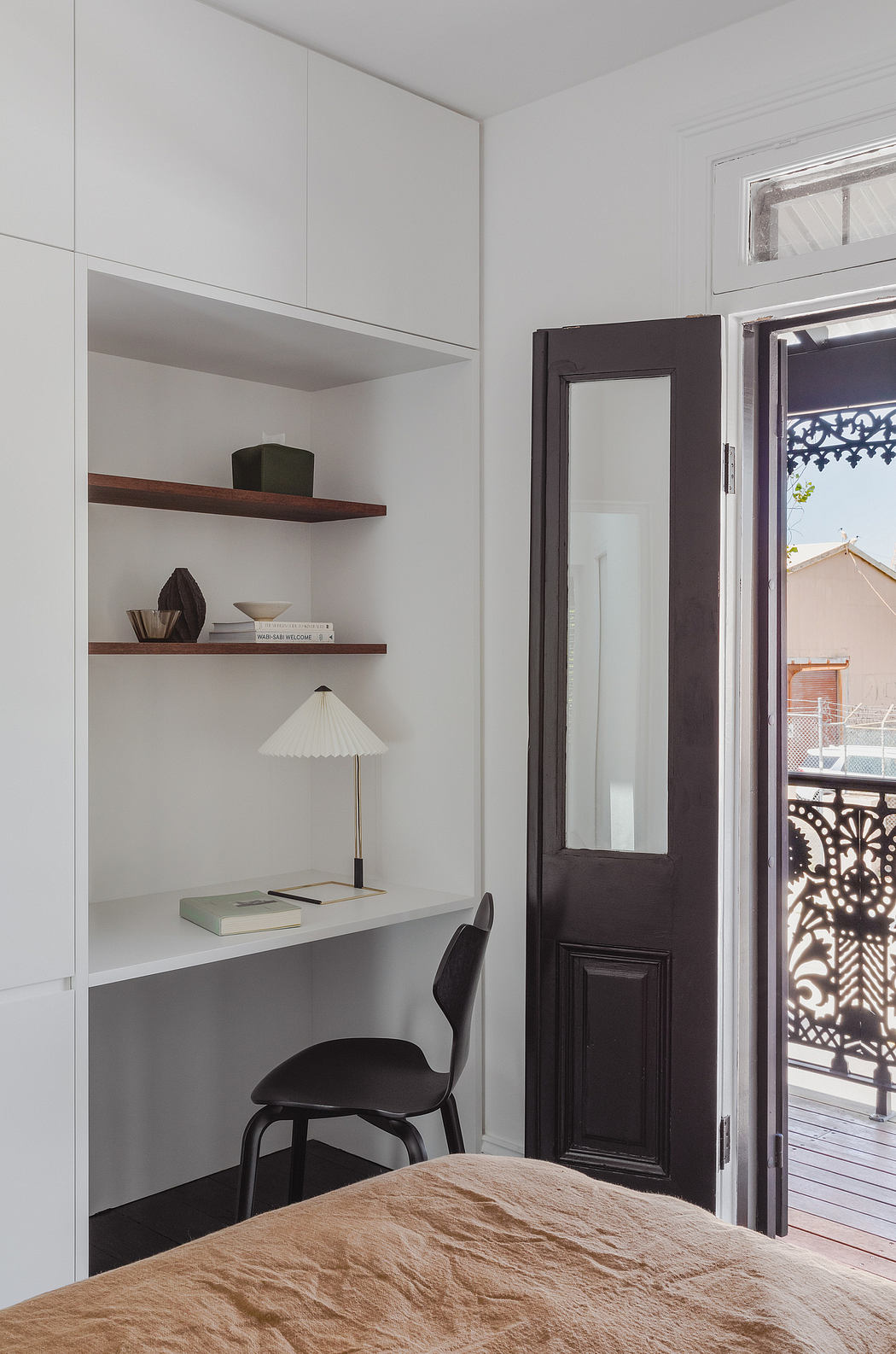 Minimalist bedroom with built-in shelving, desk, and ornate interior door. Cozy textured bedding.