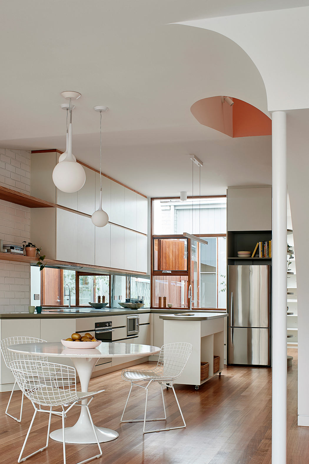 Modern kitchen with sleek cabinetry, pendant lighting, and a round dining table with wire chairs.
