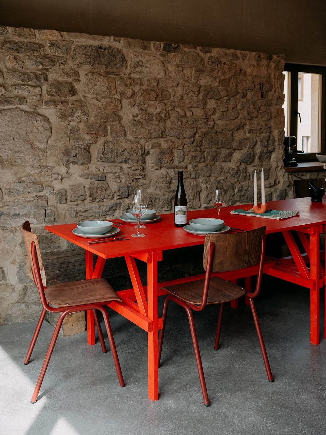 A rustic dining area with a vibrant red table and chairs contrasted against a stone wall.