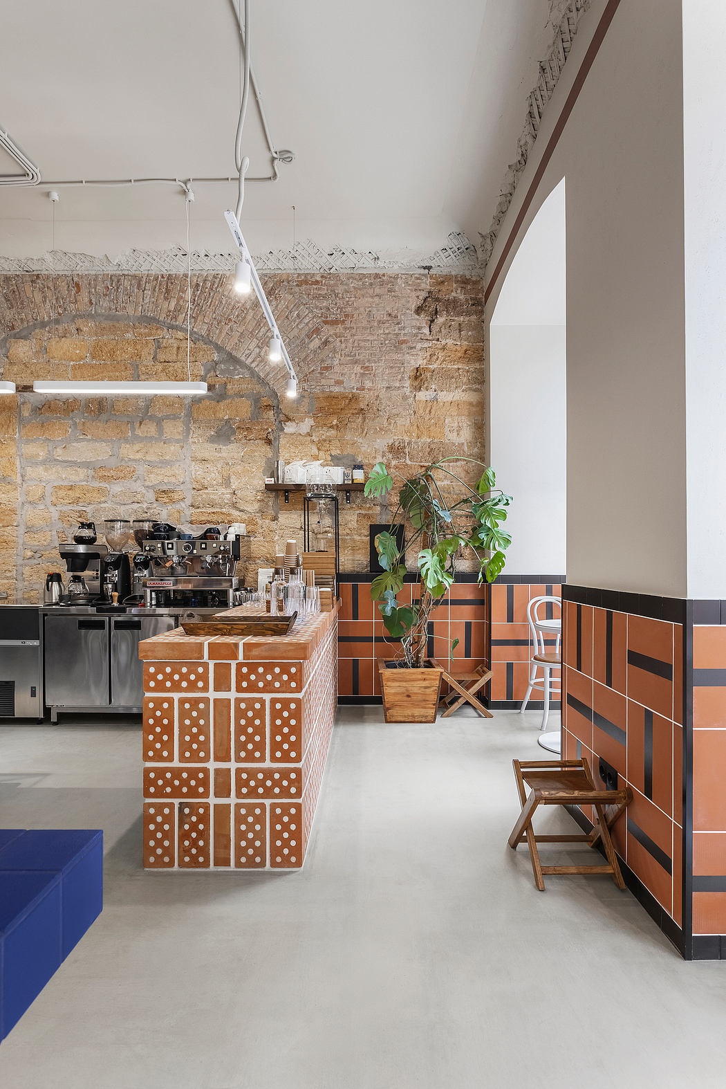 A modern, industrial-style café with exposed brick walls, geometric tiling, and potted plants.
