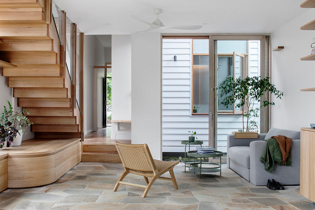 Bright, modern interior with wooden staircase, plush gray sofa, and large windows overlooking greenery.