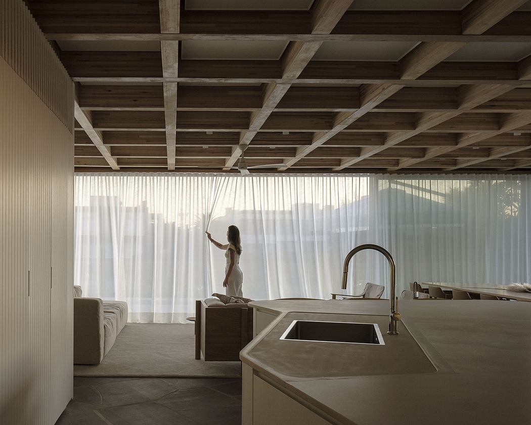 A modern, airy room with a wooden ceiling, sheer curtains, and a minimalist kitchen with concrete countertops.