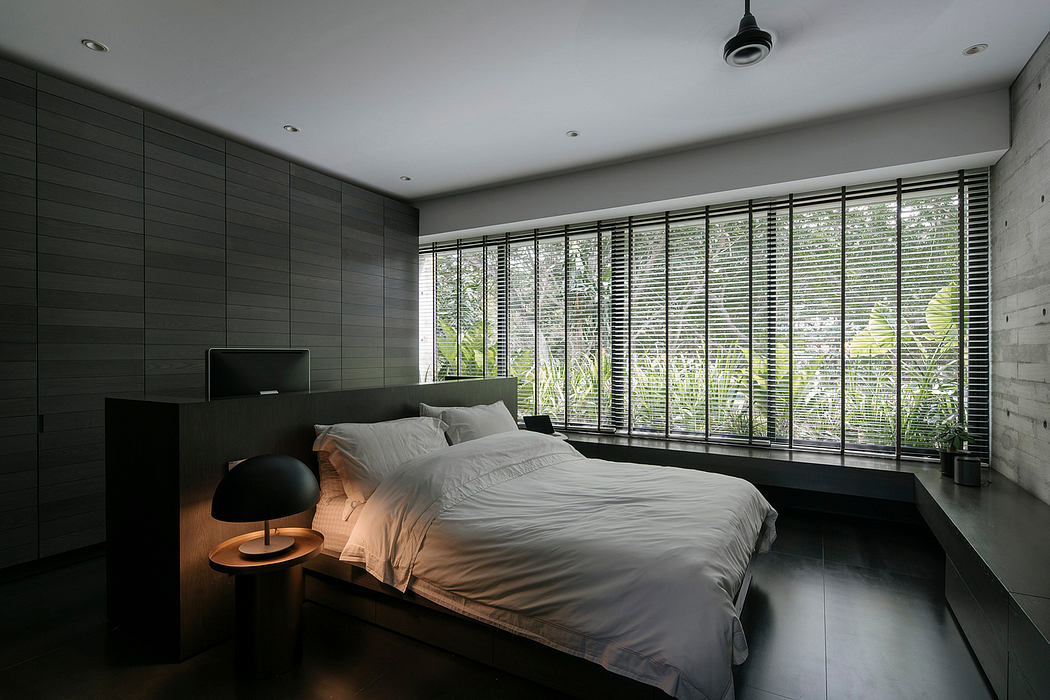 A modern, minimalist bedroom with large windows overlooking greenery. Sleek, dark decor.