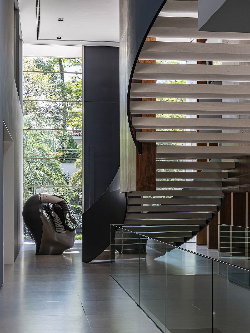 Striking spiral staircase with wood and glass design, framing lush outdoor view.