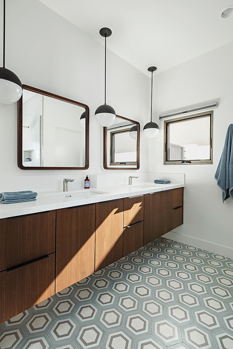 Modern bathroom with wooden vanity, geometric tile flooring, and hanging pendant lamps.
