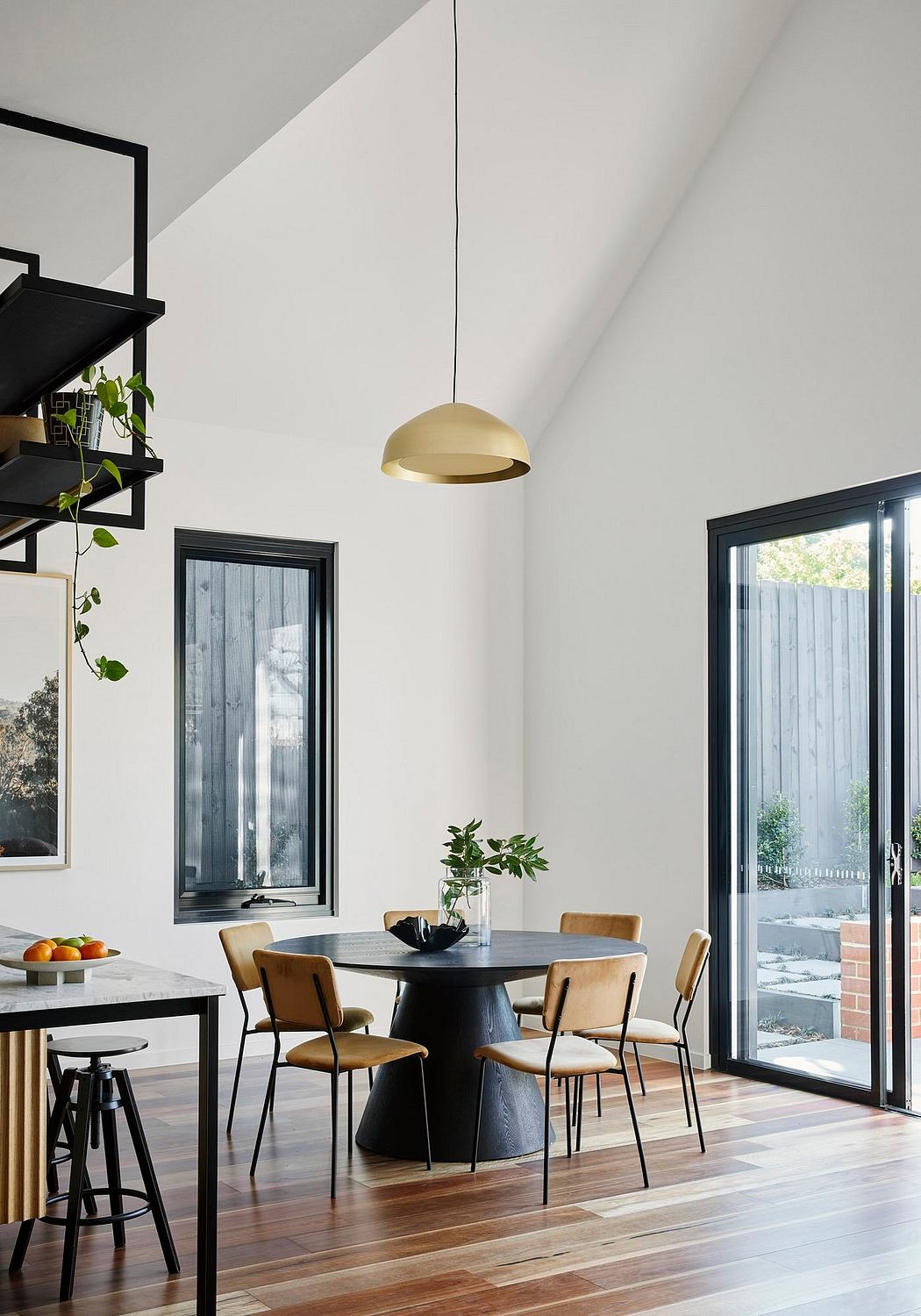 Minimalist dining area with black wood table, tan chairs, and pendant light against white walls.