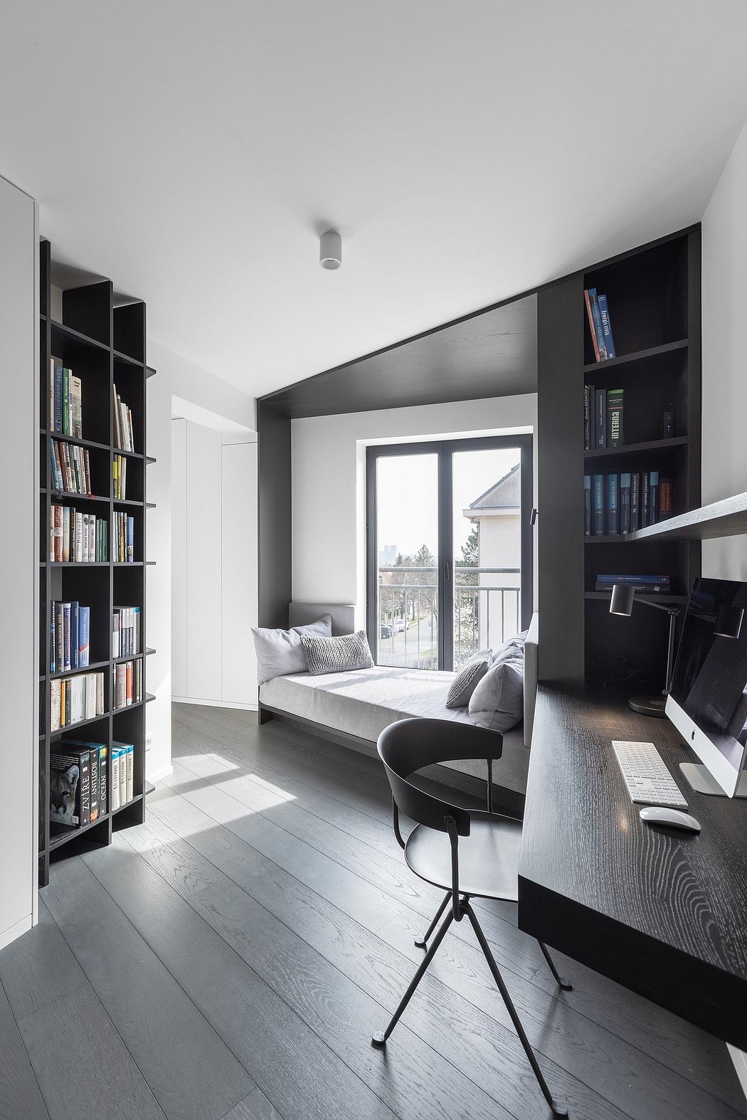 Minimalist home office with built-in bookshelves, large windows, and a cozy window seat.