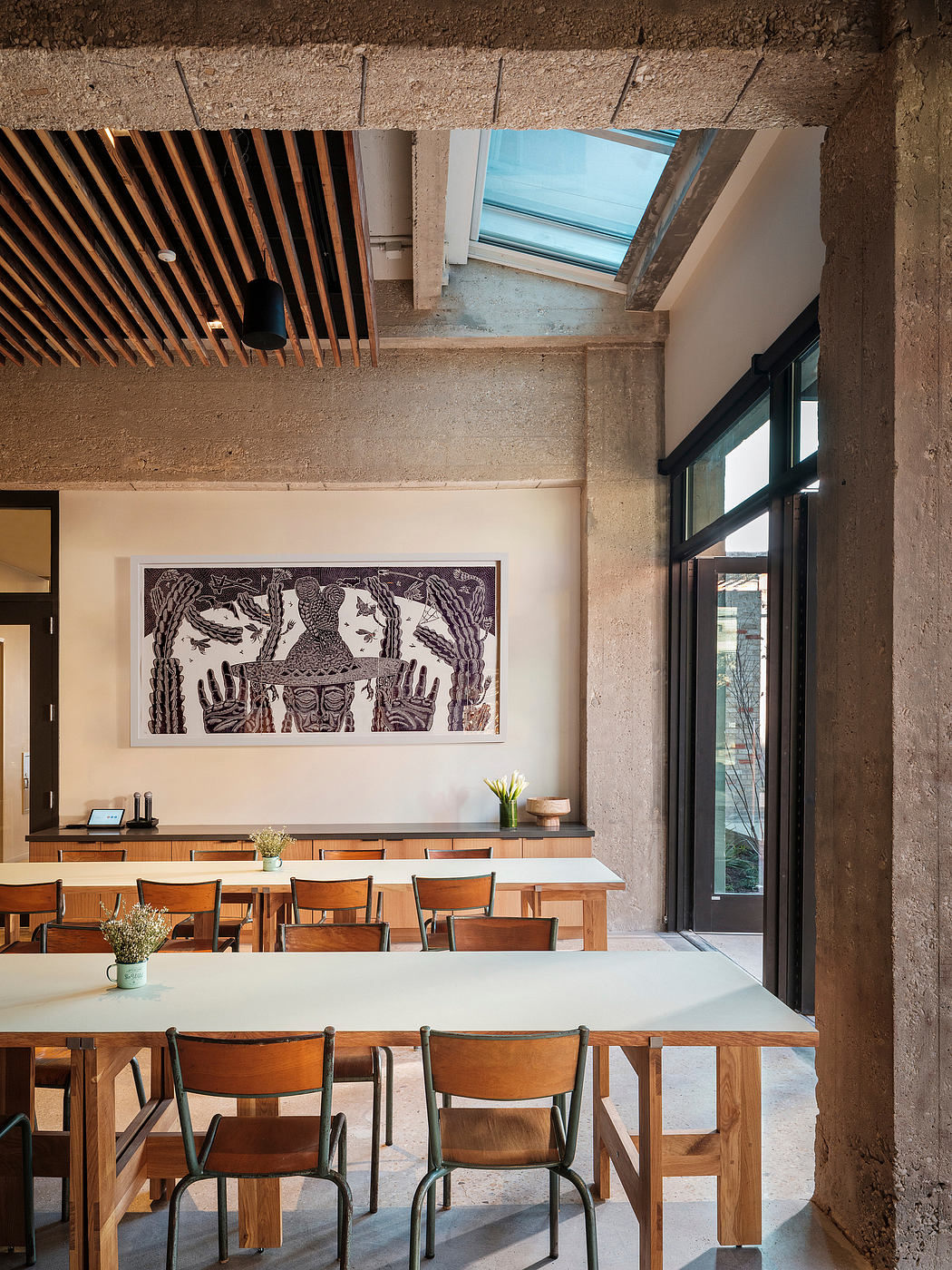 A cozy industrial-style cafe with wooden furniture, concrete walls, and a striking artwork.