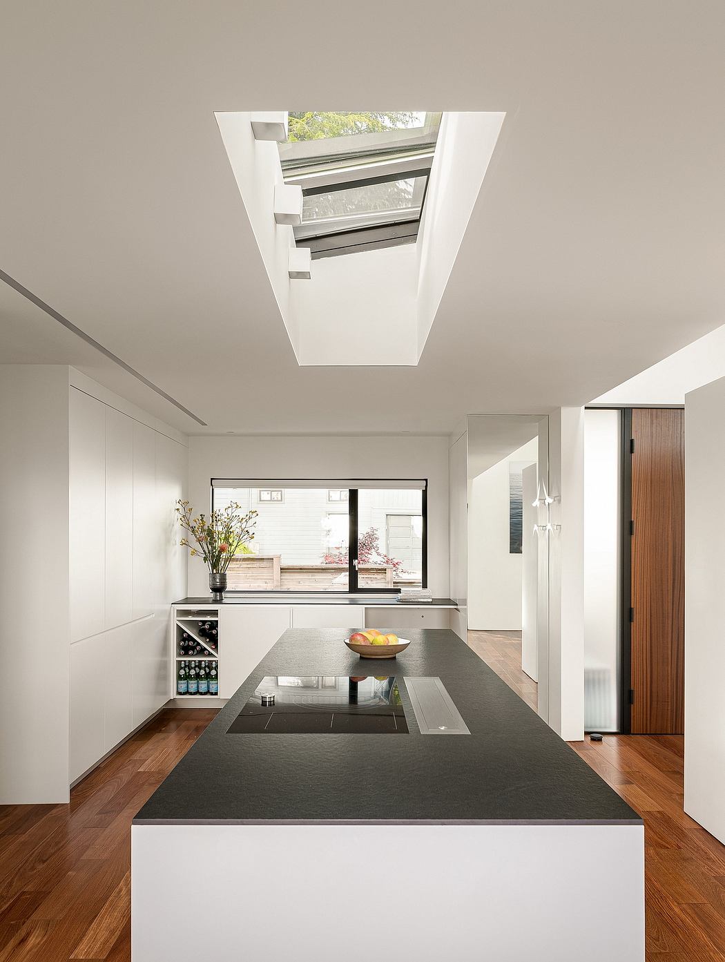 Minimalist kitchen with sleek black countertop, wooden floors, and natural light from skylight.