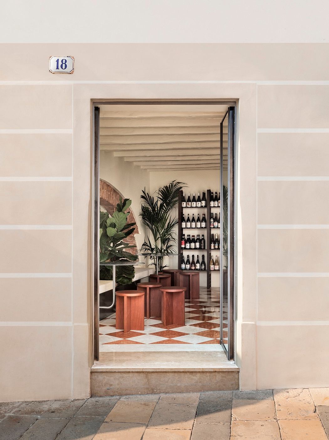 Inviting entryway with wooden shelves displaying wine bottles, surrounded by tiles and potted plants.