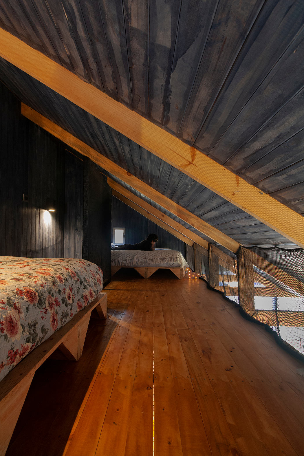 Cozy attic space with rustic wooden beams, colorful bed linens, and warm lighting.