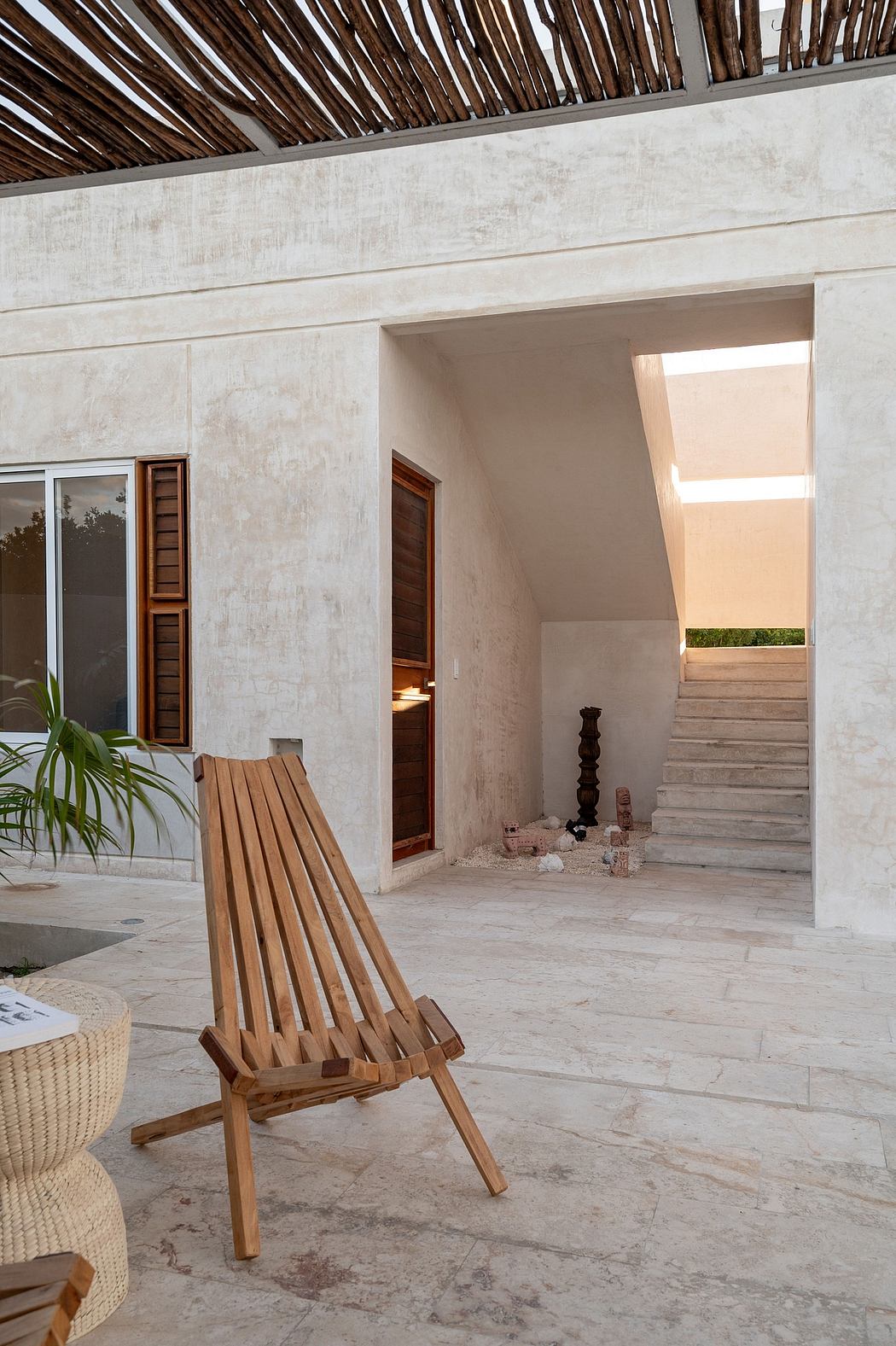 A minimalist architectural space with wooden seating, concrete walls, and a thatched roof.