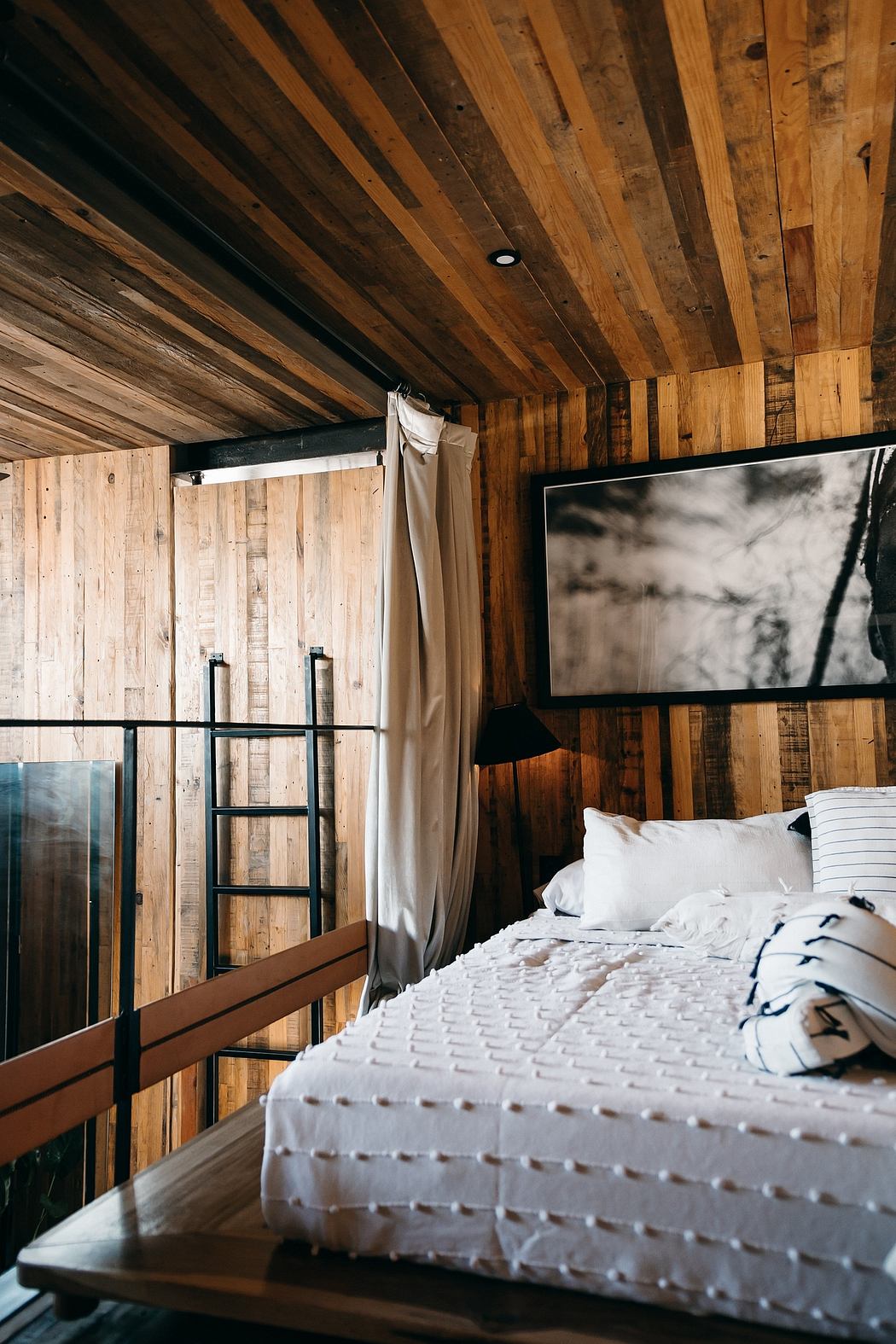 Rustic cabin interior with wooden paneled walls, large bed, and black-and-white artwork.
