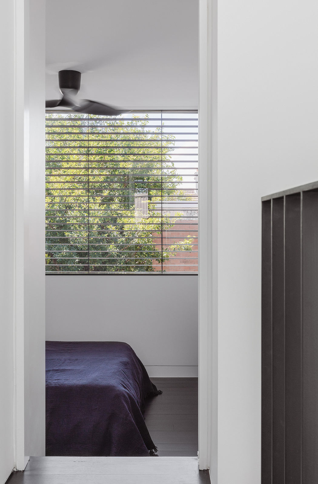 A contemporary bedroom with a view of lush greenery through slatted blinds and minimalist decor.