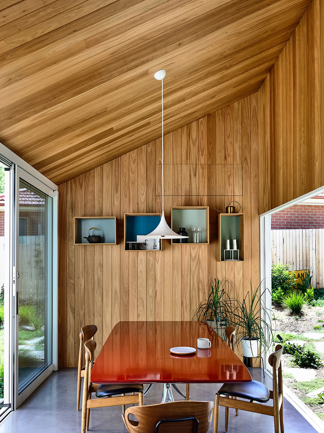 A cozy wooden dining room with built-in shelving units and a vibrant red table.