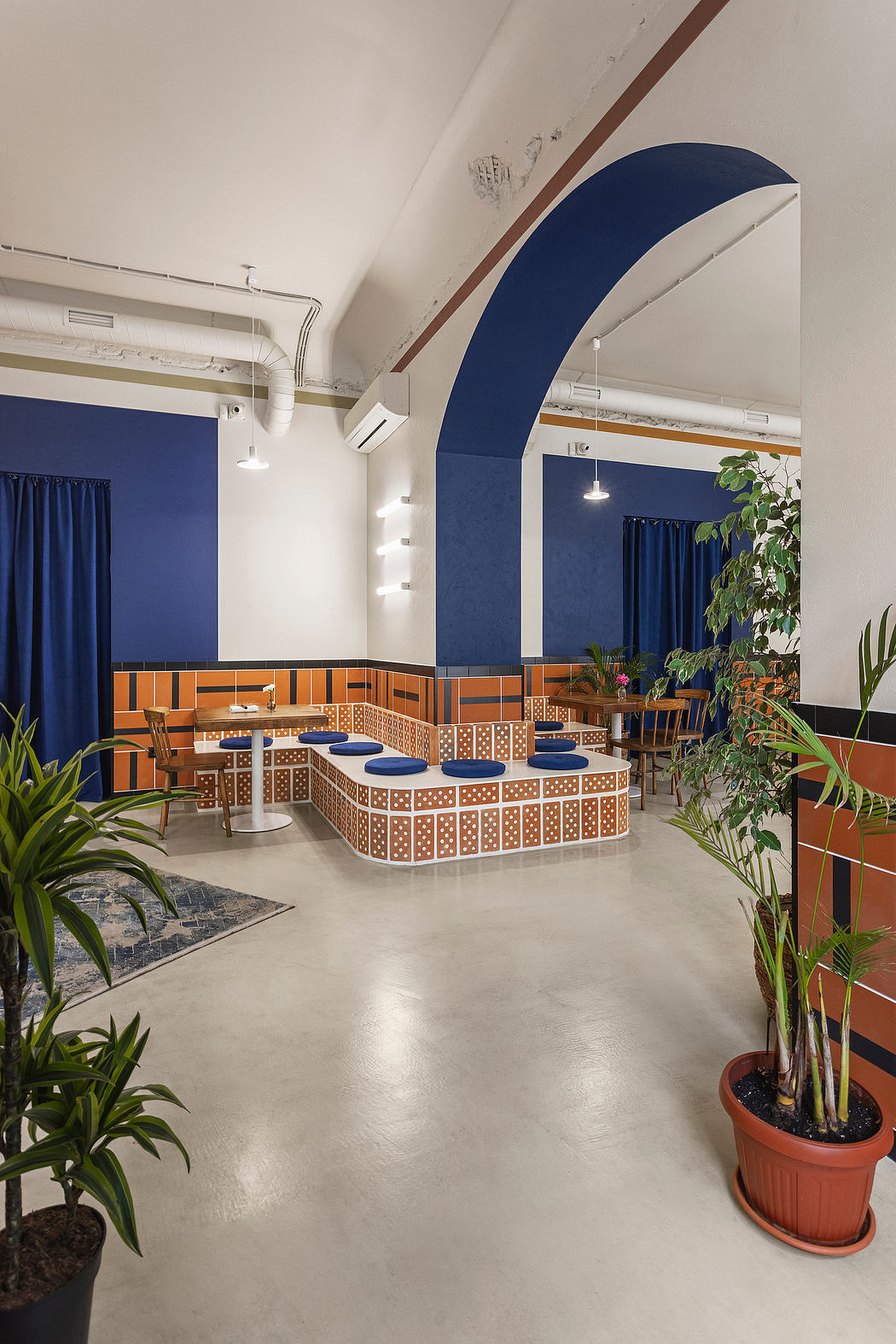 Vibrant blue and orange color scheme, intricate tiled seating area, lush indoor plants.