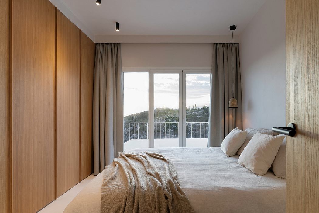 Spacious bedroom with large windows, wood paneled walls, and a balcony overlooking a scenic vista.