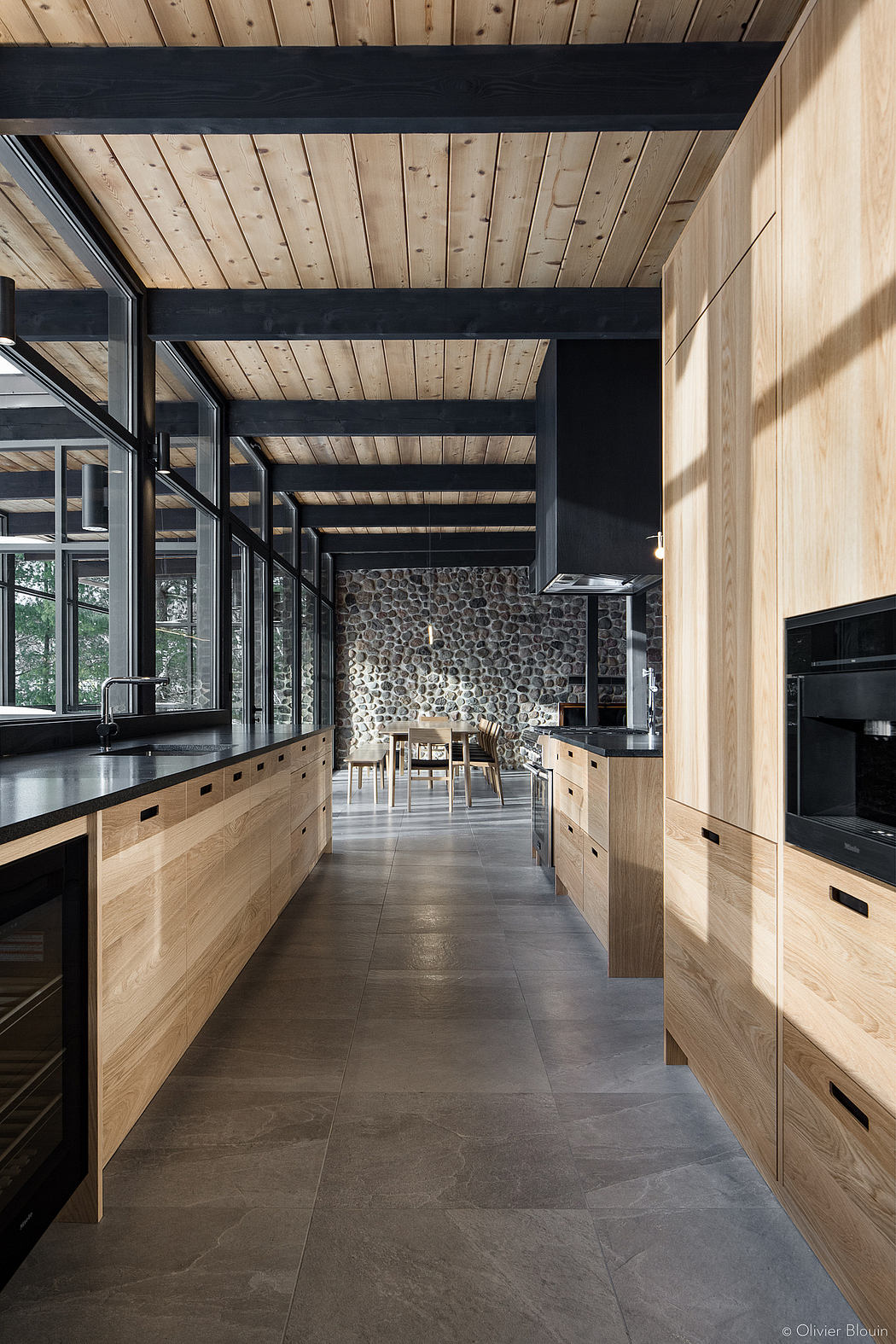 Rustic kitchen with exposed wooden beams, stone wall, and sleek black countertops.