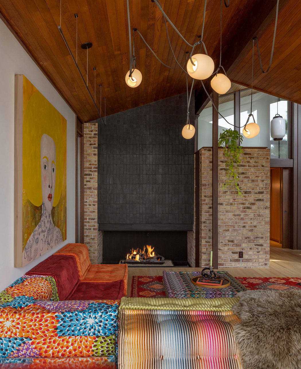 A cozy, eclectic living room with a brick fireplace, hanging pendant lights, and vibrant furnishings.